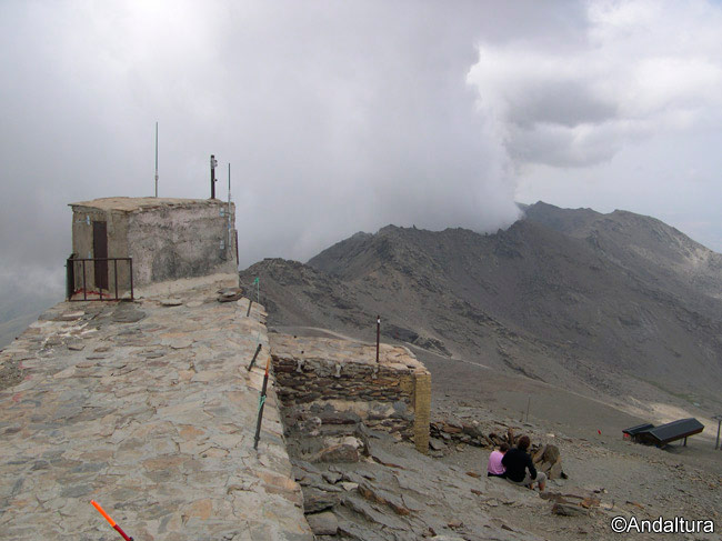 Caseta en la cumbre del Veleta, al fondo, entre nubes, los Tajos de la Virgen y del Nevero